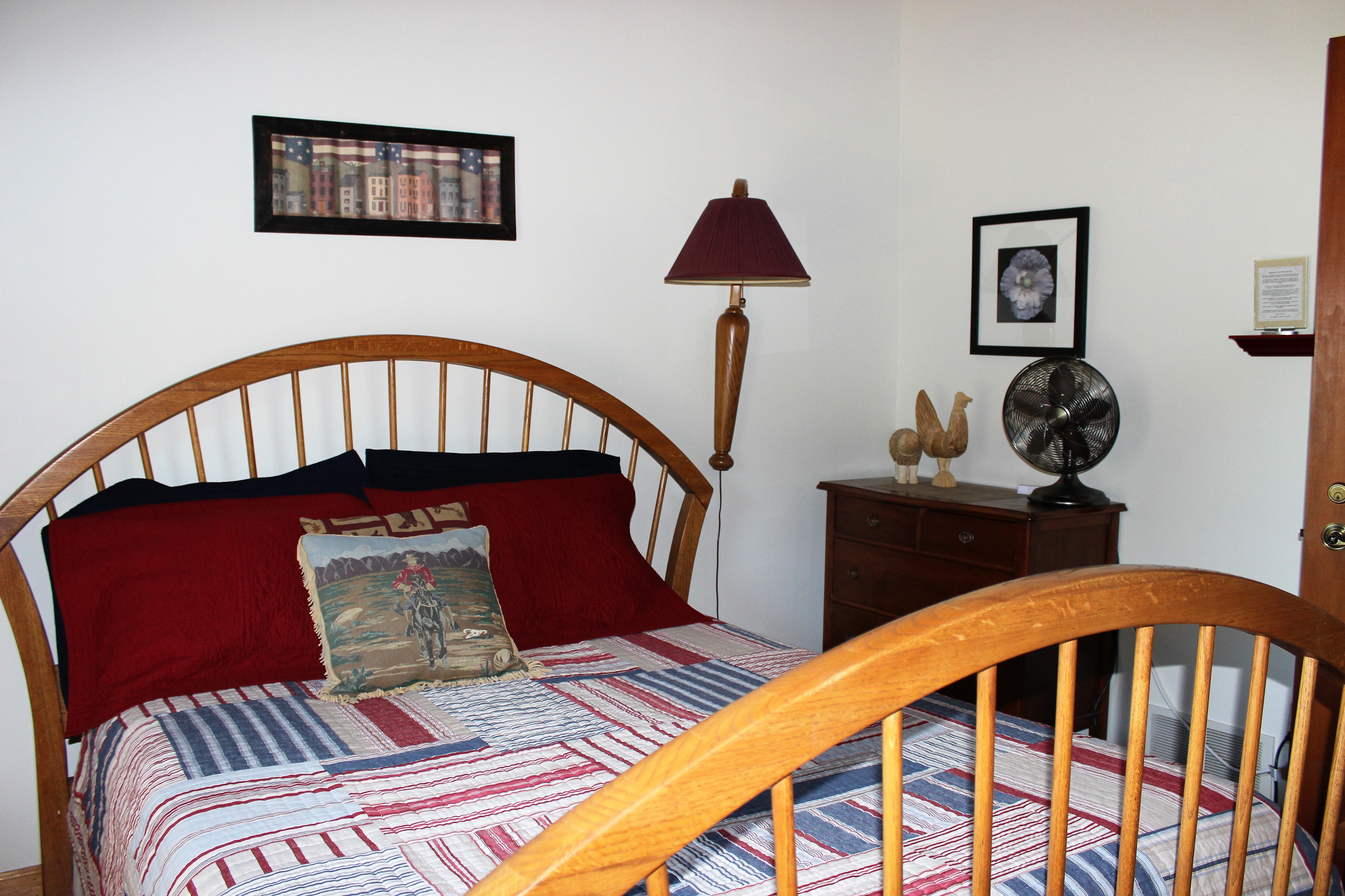 Queen sized wooden spindle bed covered with red, white and blue patchwork quilt
