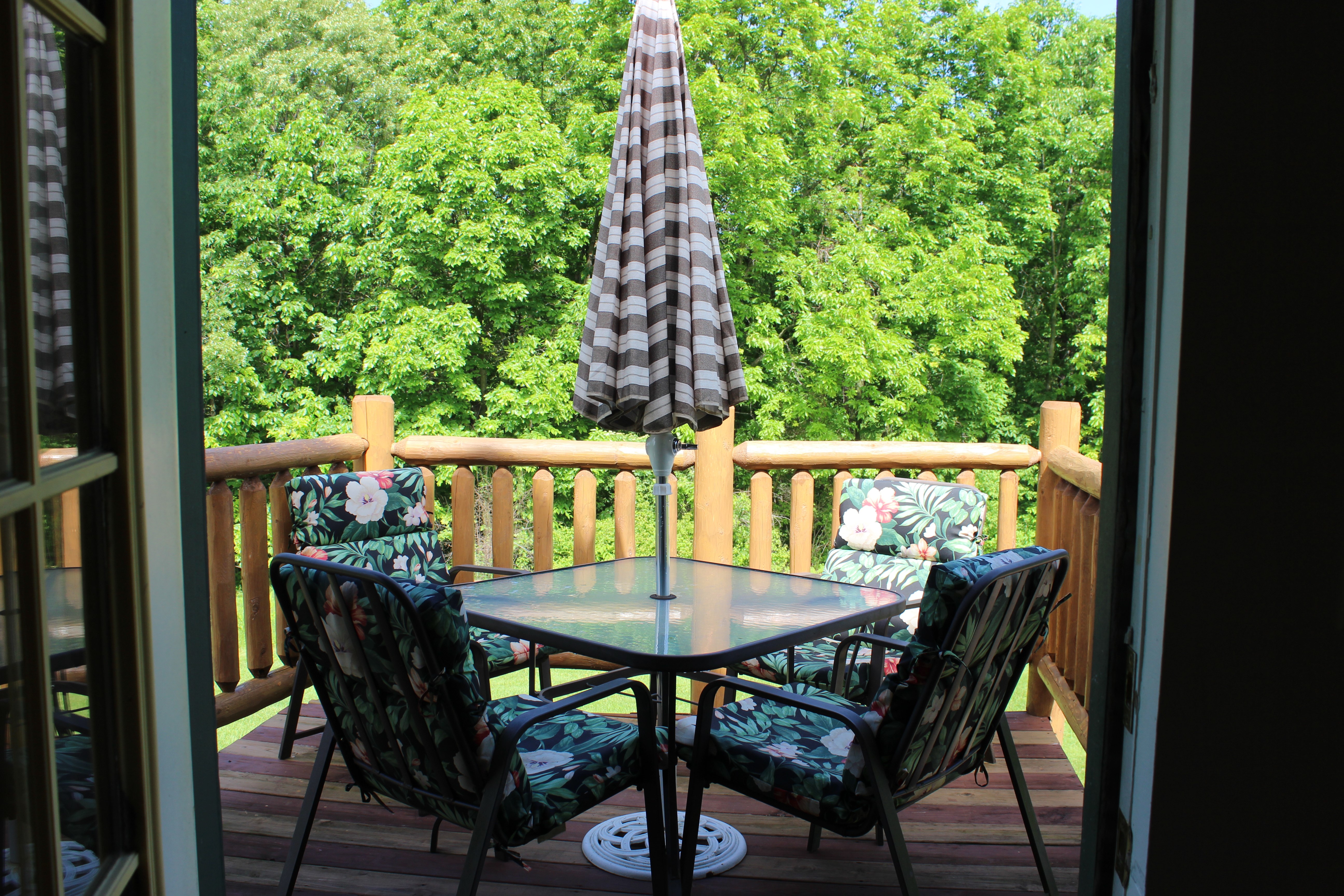 View from door of private deck, glass patio table, umbrella and 4 cushioned chairs.