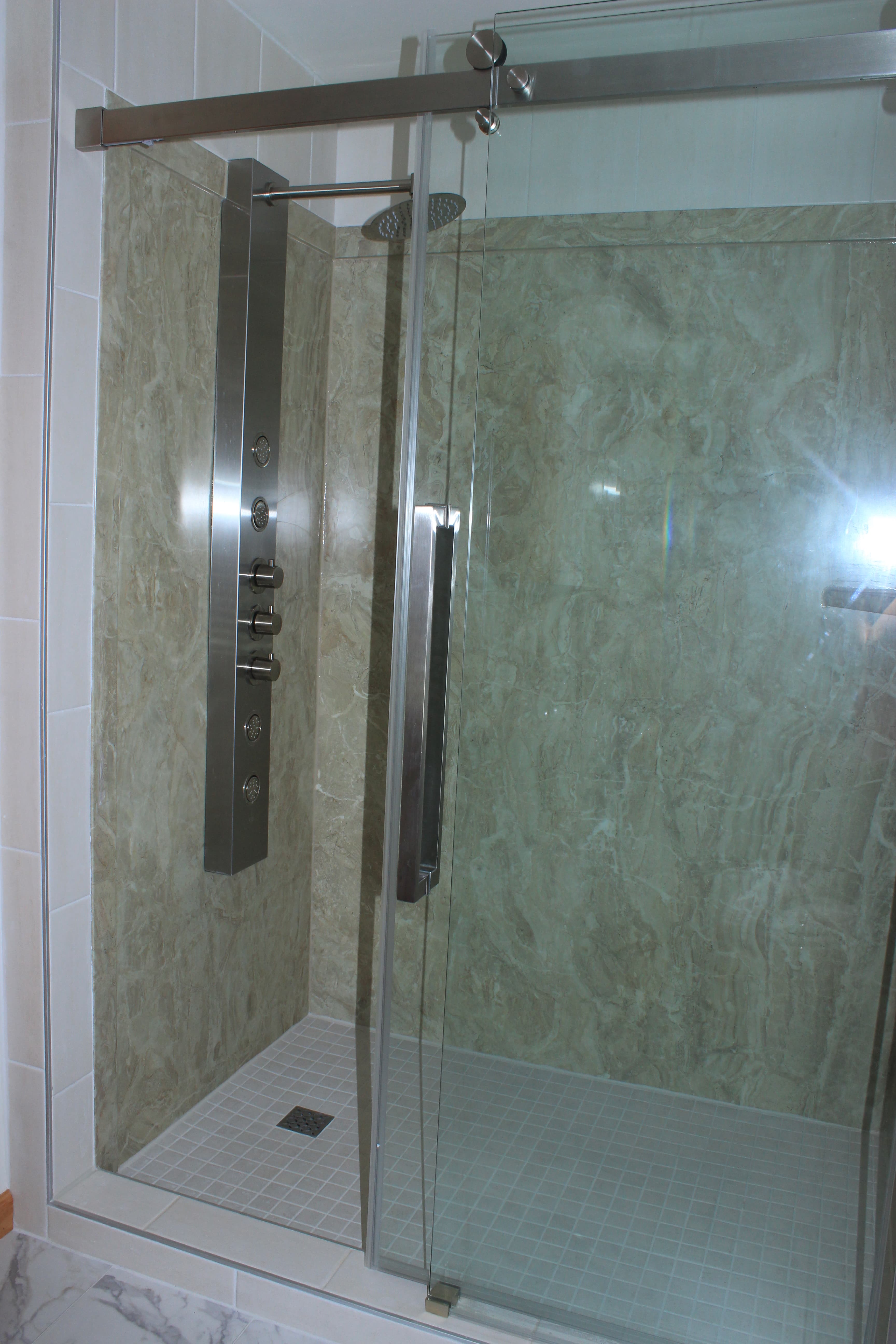 Modern walk-in hydrotherapy shower with a sliding glass door. The interior walls are finished with light green marble-patterned tiles, and the floor has a small white mosaic tile design.