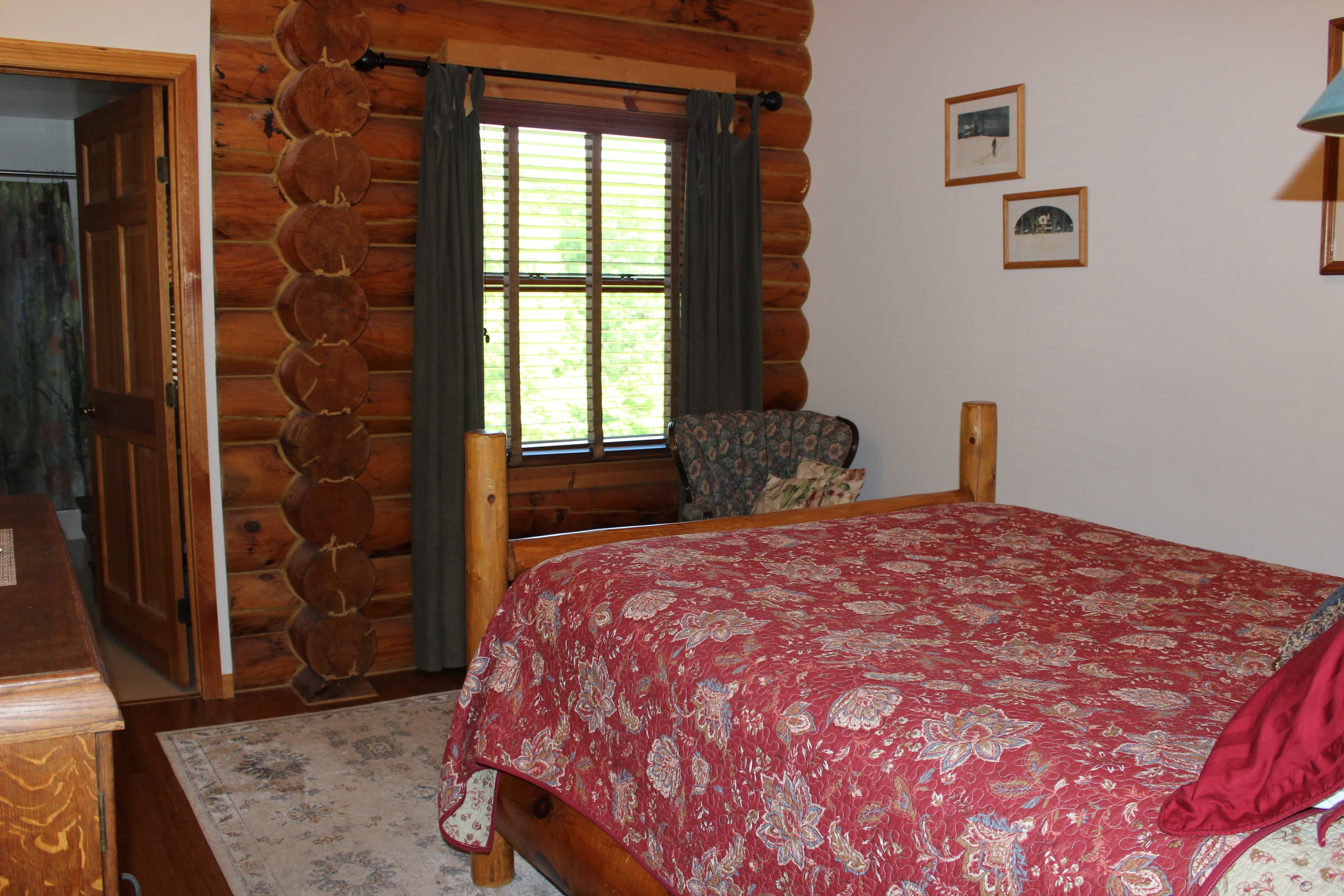Queen sized log bed with burgundy floral quilt, set on white area rug and hardwood floor.