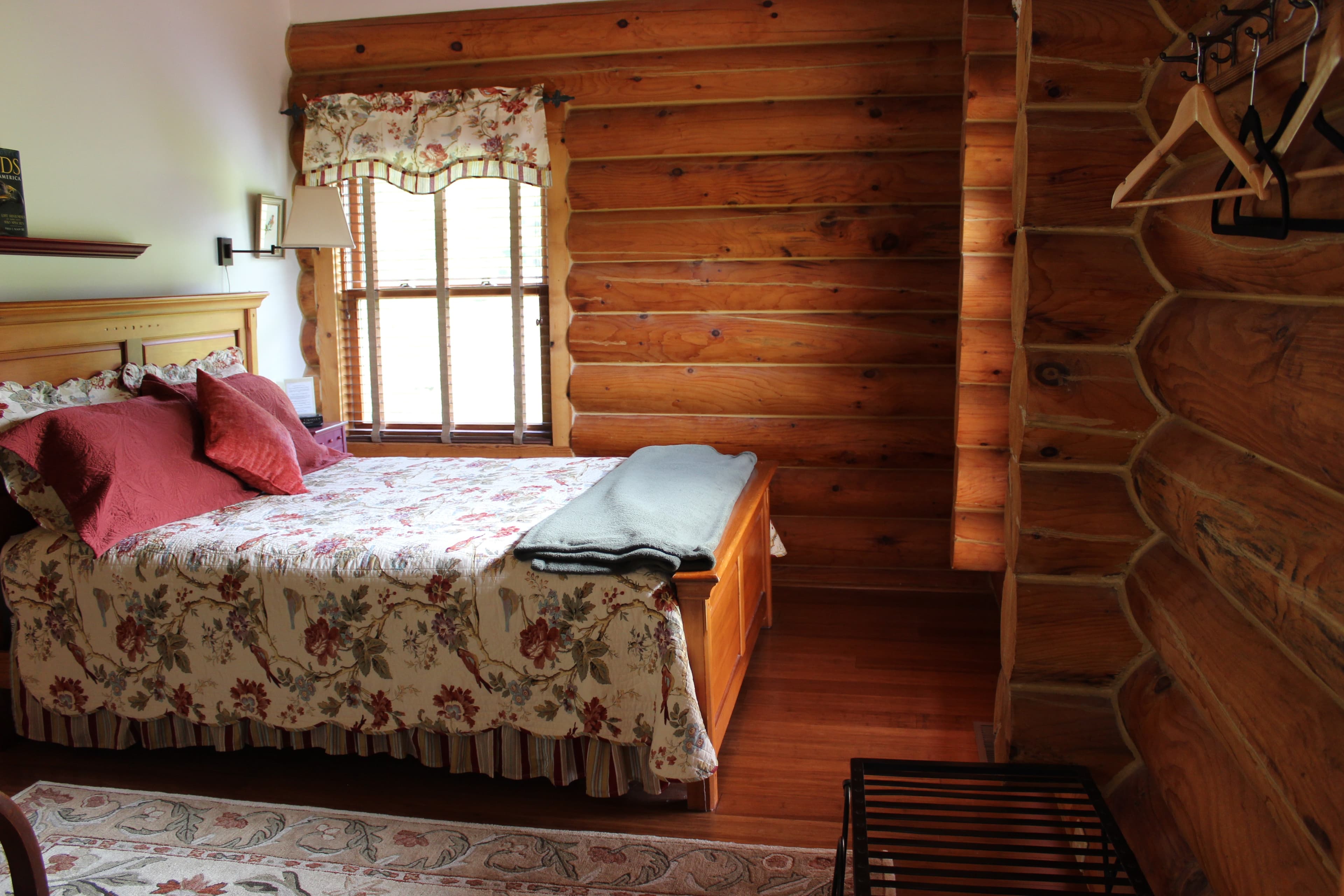 Queen sized bed with bird themed bedding, hardwood floors, log walls.