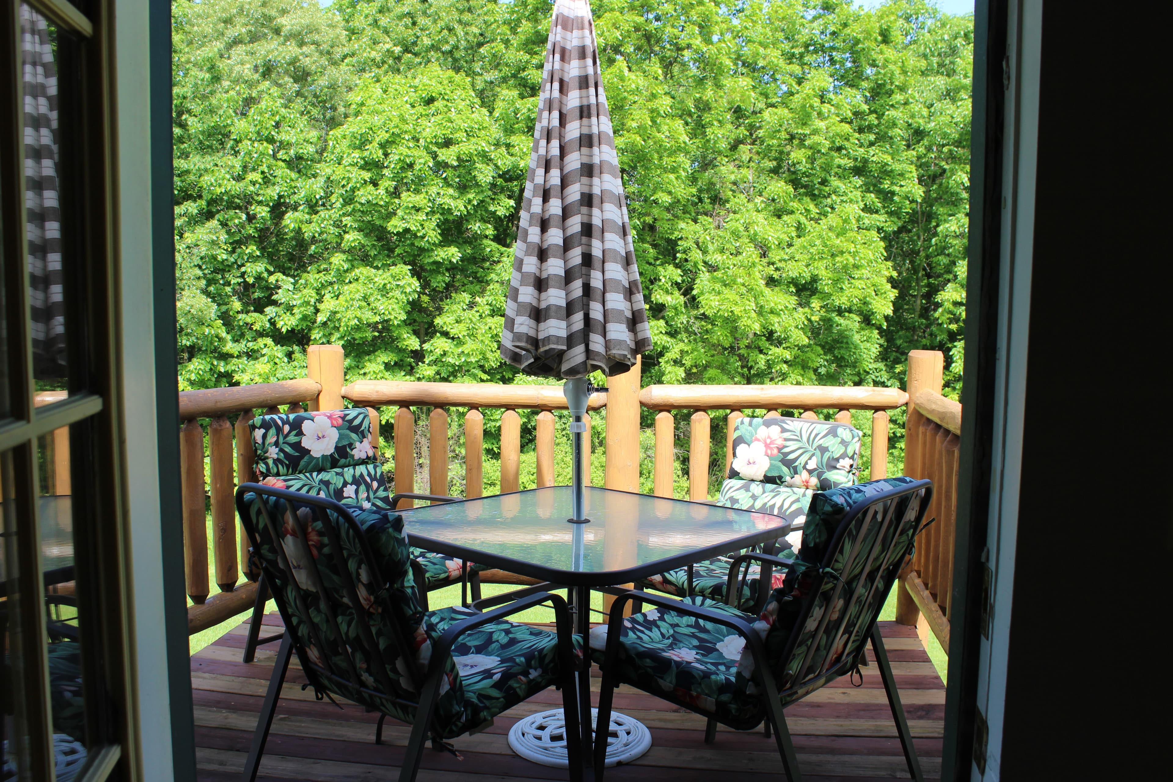 View from door of private deck, glass patio table, umbrella and 4 cushioned chairs.