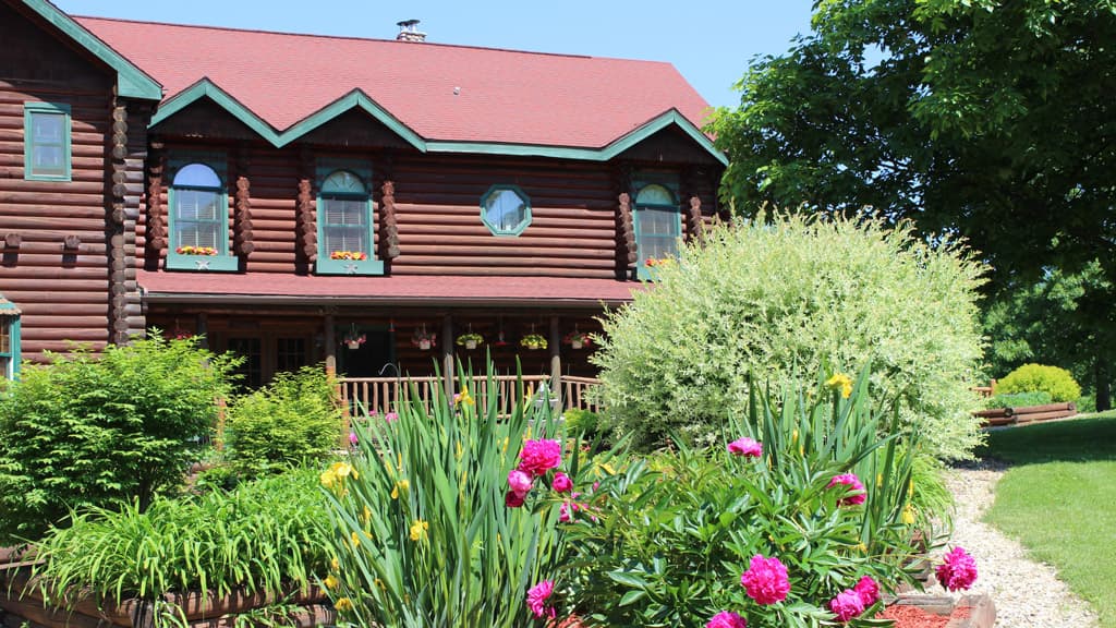 A log cabin with a red roof surrounded by lush greenery and colorful flowers. A log cabin with a red roof surrounded by lush greenery and colorful flowers.