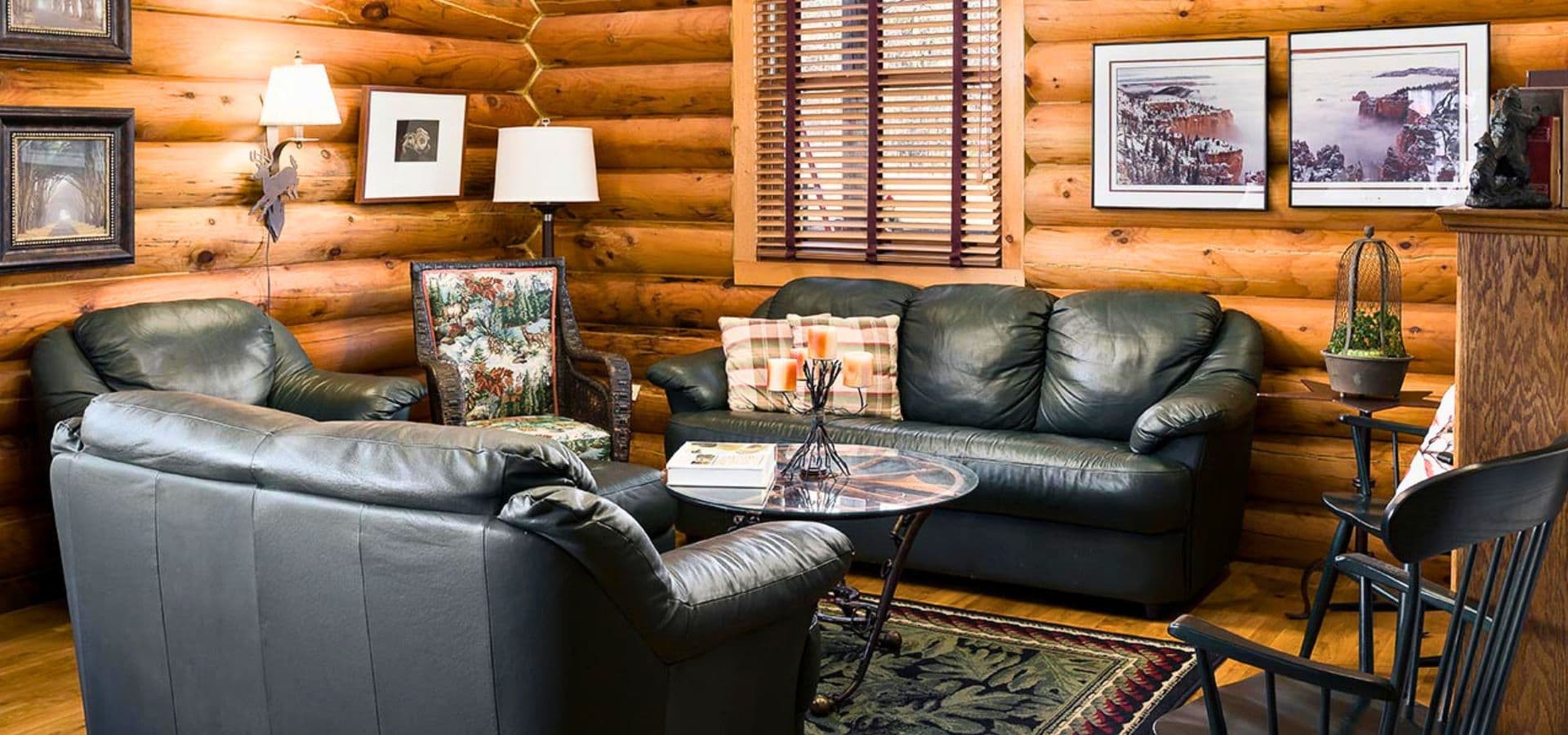 A cozy living room with leather sofas, a glass coffee table, and wooden log walls embellished with art.