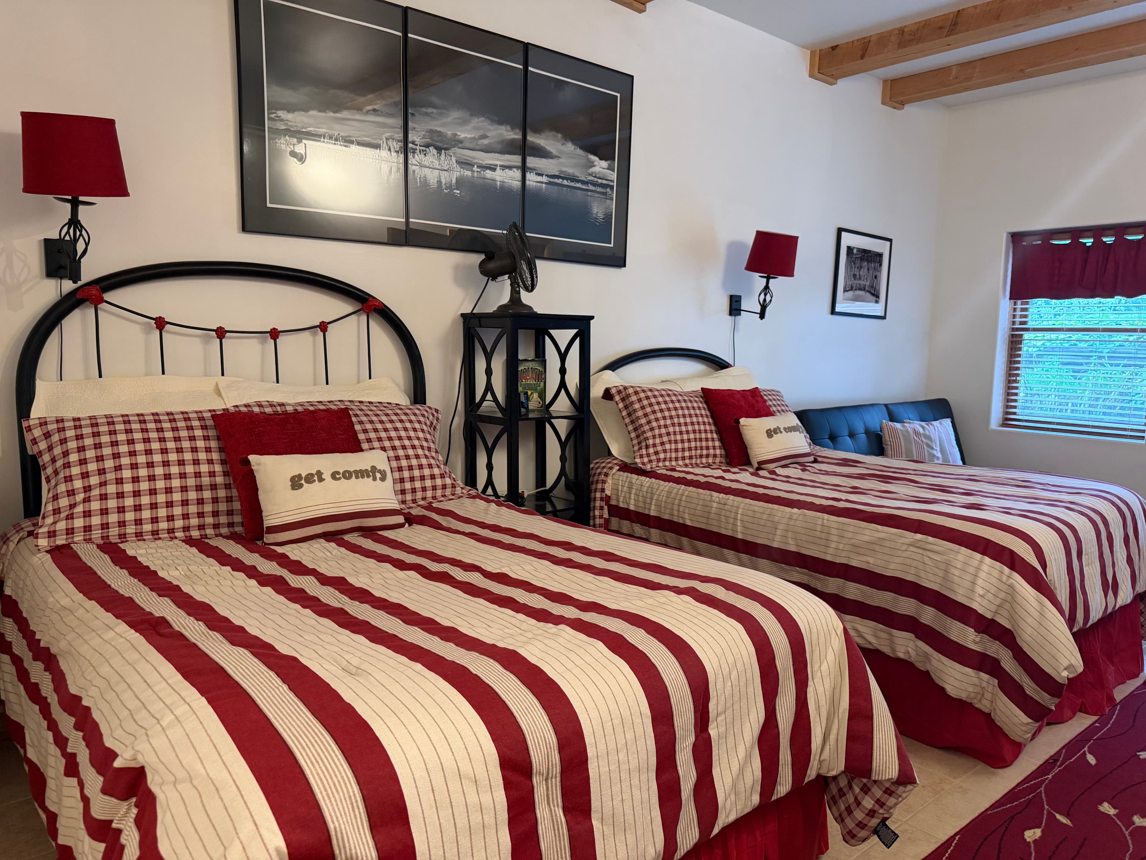 A cozy bedroom featuring two beds with red and white striped bedding, wall art, and soft lighting.