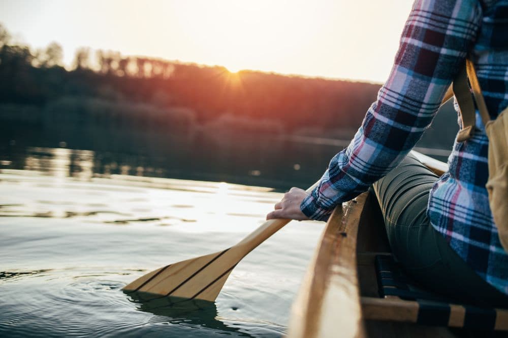 A person paddles in a canoe on a calm lake during sunset.
