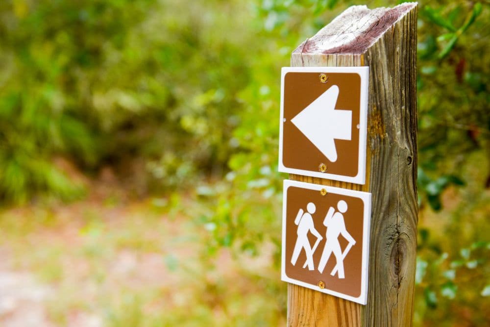 A wooden trail sign indicating a left turn and showing hiker symbols.