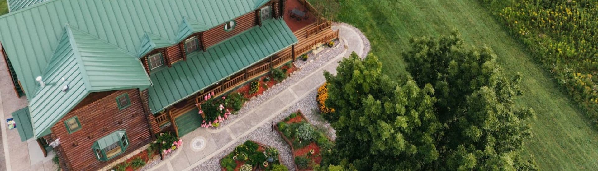 Aerial view of a log cabin with a green roof surrounded by landscaped gardens.
