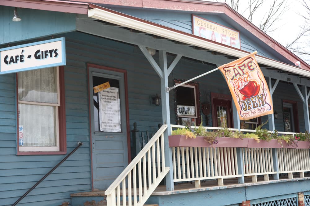 A blue, two-story building featuring a café and gift shop with an "Open" sign and hanging flower pots.