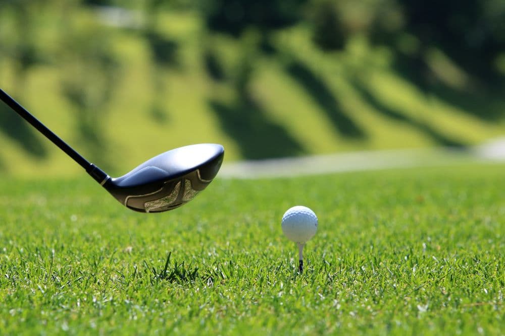 A golf club is poised to strike a white golf ball on a grassy fairway.