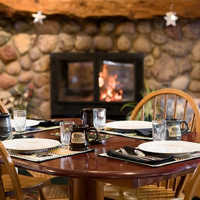 A rustic dining table set with plates, glassware, and cutlery against a stone fireplace backdrop.