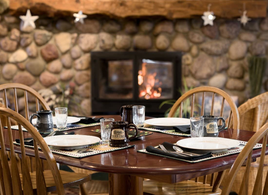 A cozy dining table set for a meal, with plates and mugs, in front of a stone fireplace.