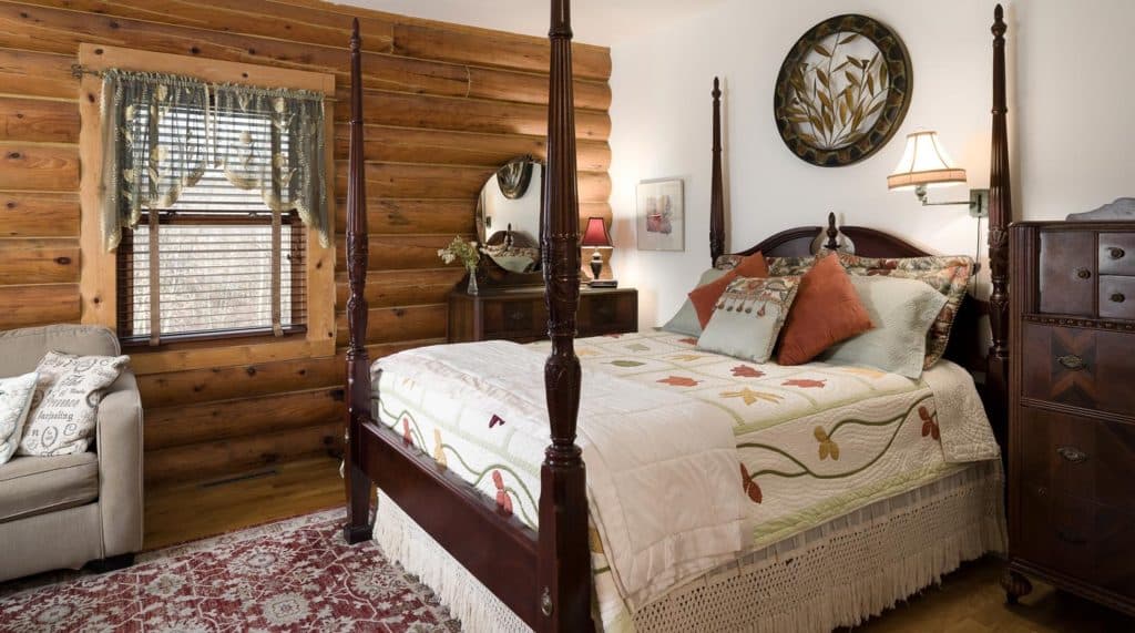 A cozy cabin bedroom featuring a four-poster bed, decorative pillows, and wooden walls.