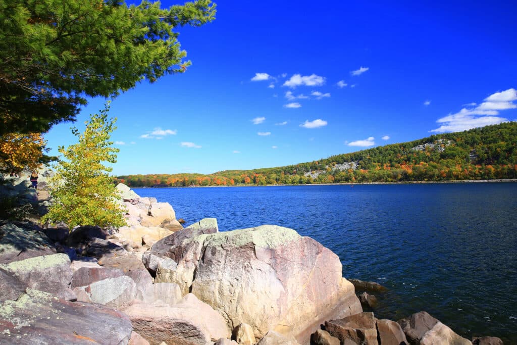 A serene lakeside scene featuring rocky shores, colorful trees, and a clear blue sky.