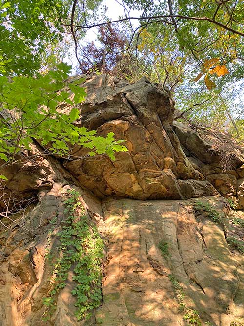 A rugged rock formation partially covered with greenery under a bright sky.