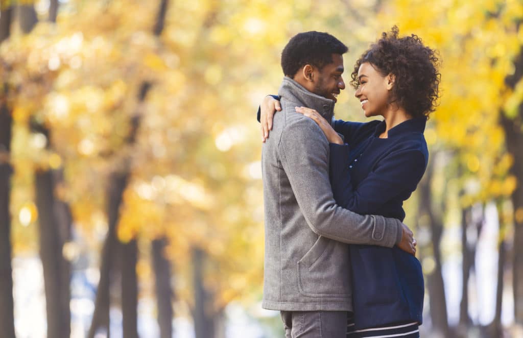 A couple embraces and smiles at each other in an autumn park.