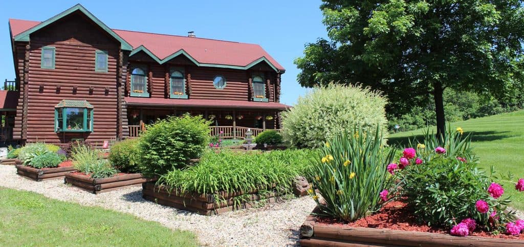 A log cabin with a red roof surrounded by colorful flower beds and green landscaping. A log cabin with a red roof surrounded by colorful flower beds and green landscaping.