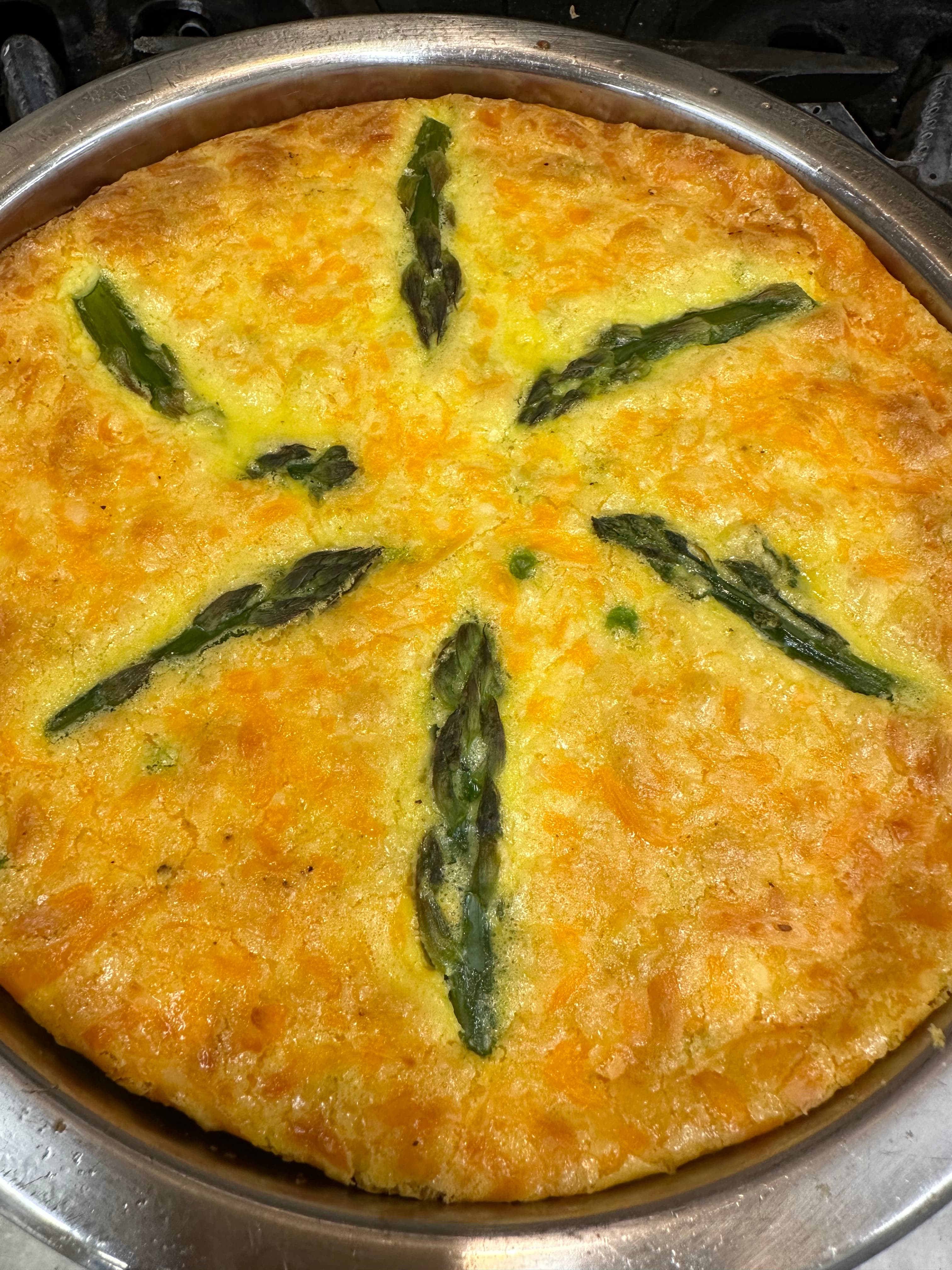 A golden baked frittata topped with asparagus spears arranged in a star pattern.