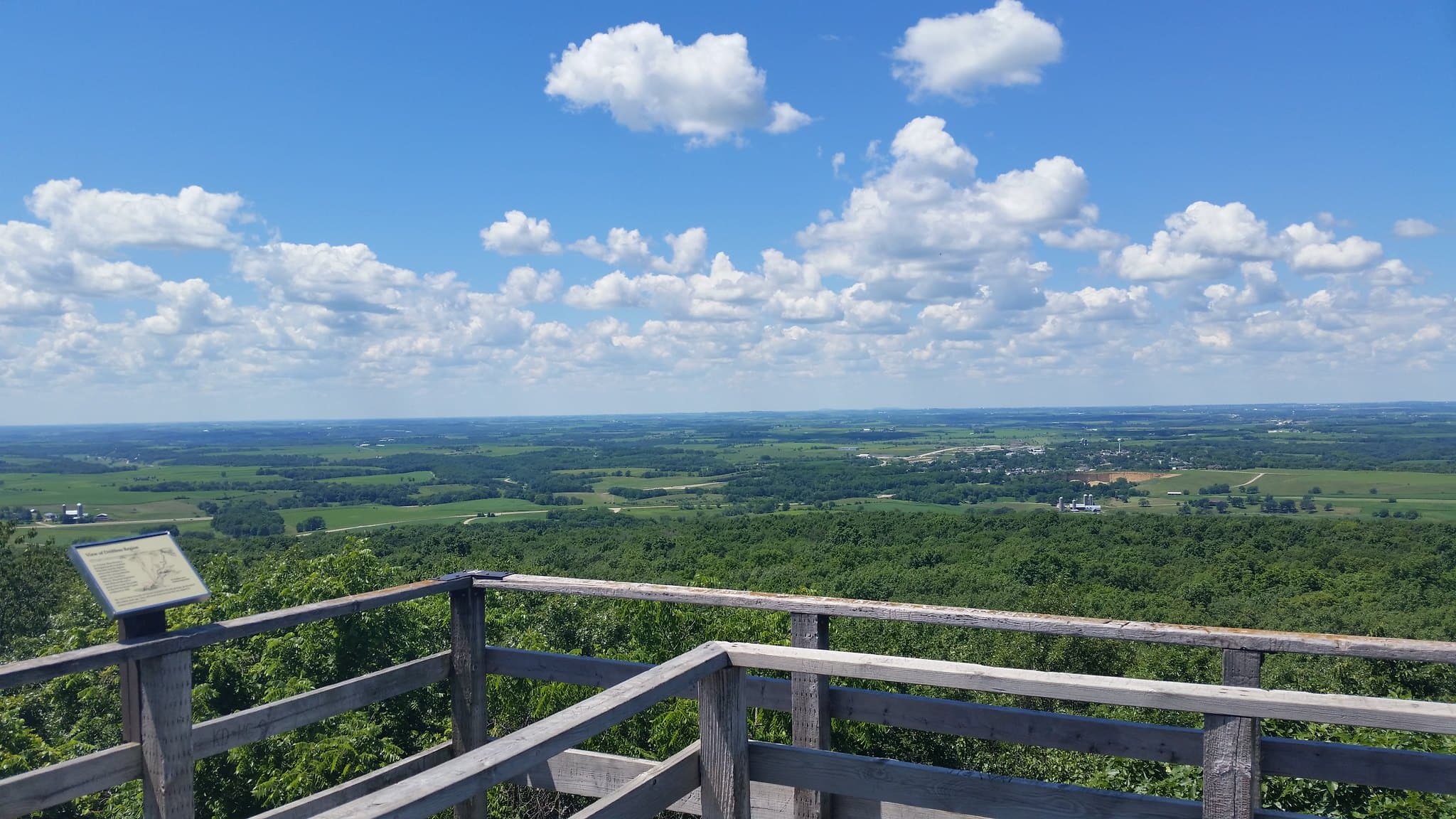 Panoramic view of lush green hills and a bright blue sky with clouds from a wooden observation deck. Panoramic view of lush green hills and a bright blue sky with clouds from a wooden observation deck.
