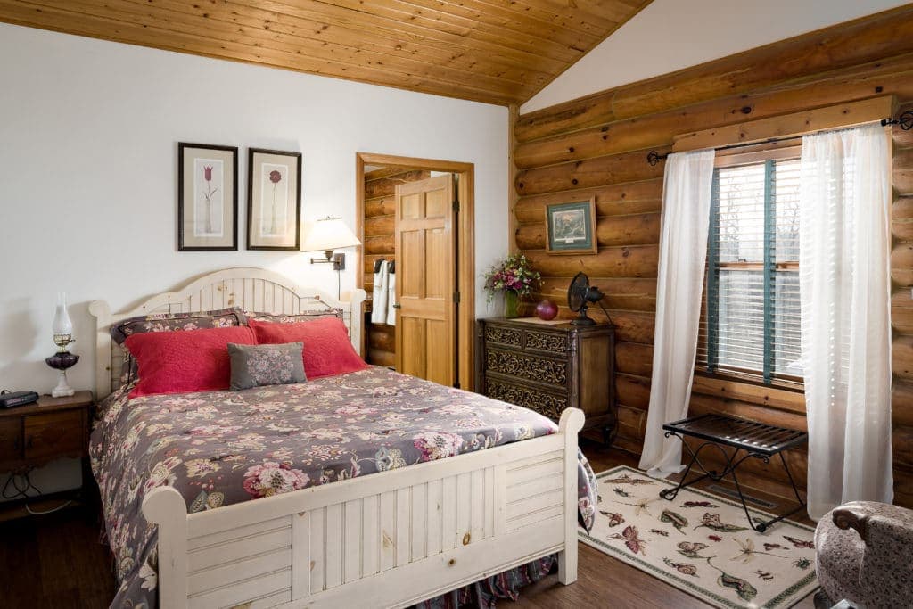 A cozy bedroom with a wooden ceiling, a floral-patterned bedspread, and rustic decor.