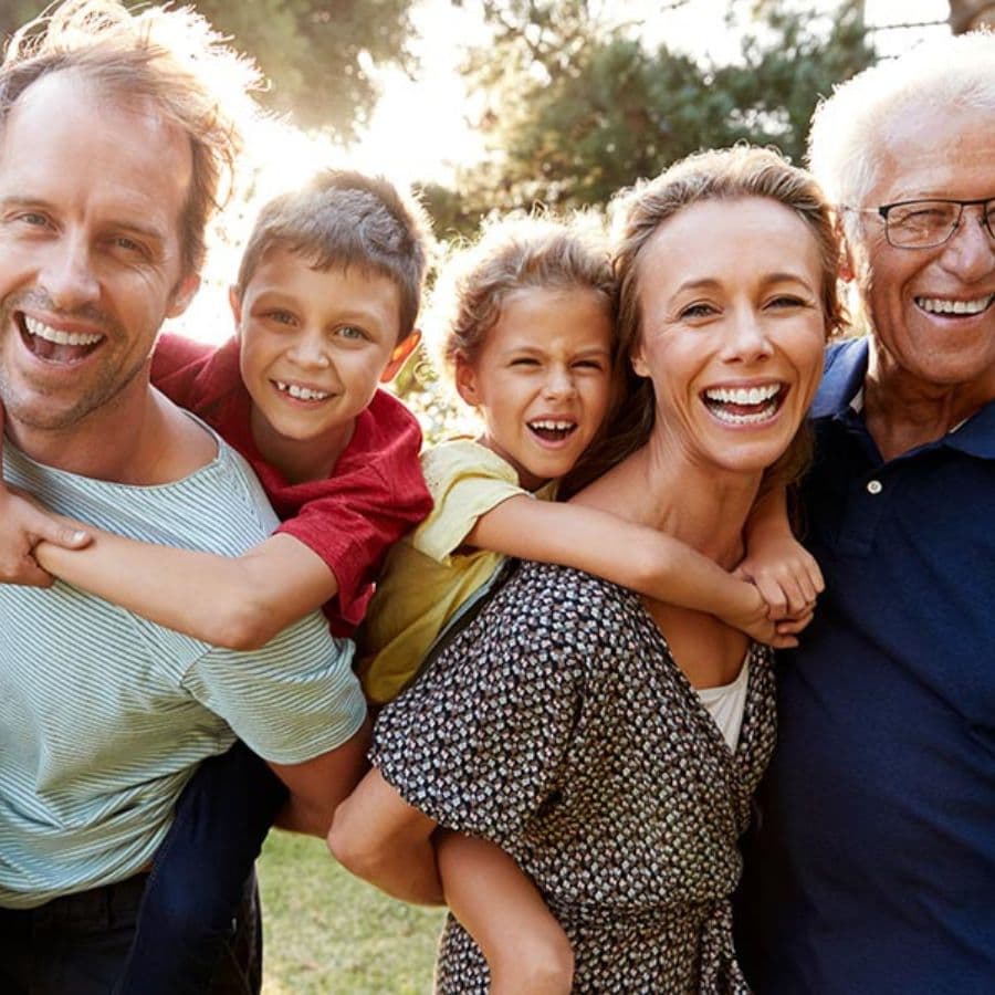 A joyful family of five, including two adults and three children, smiling together outdoors.