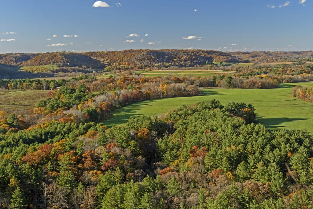 A panoramic view of rolling hills and vibrant autumn foliage in a rural landscape.